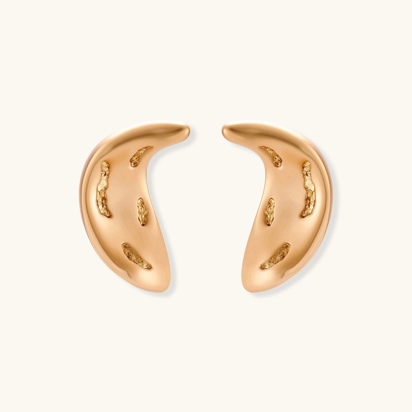 Pair of gold crescent moon-shaped stud earrings with textured surface details on cream background.