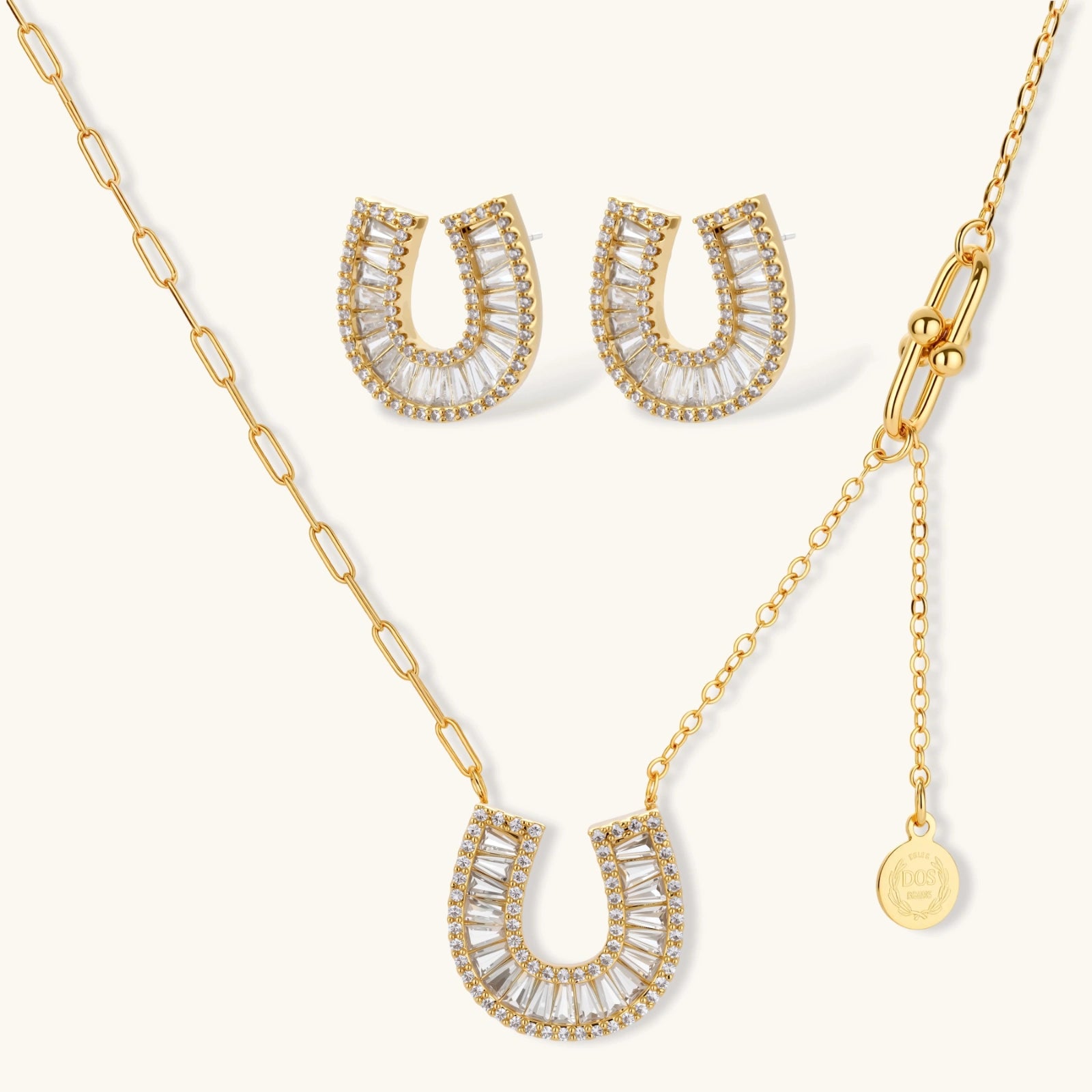 Gold-plated horseshoe necklace and earring set with baguette and round crystals arranged in geometric pattern on white background.