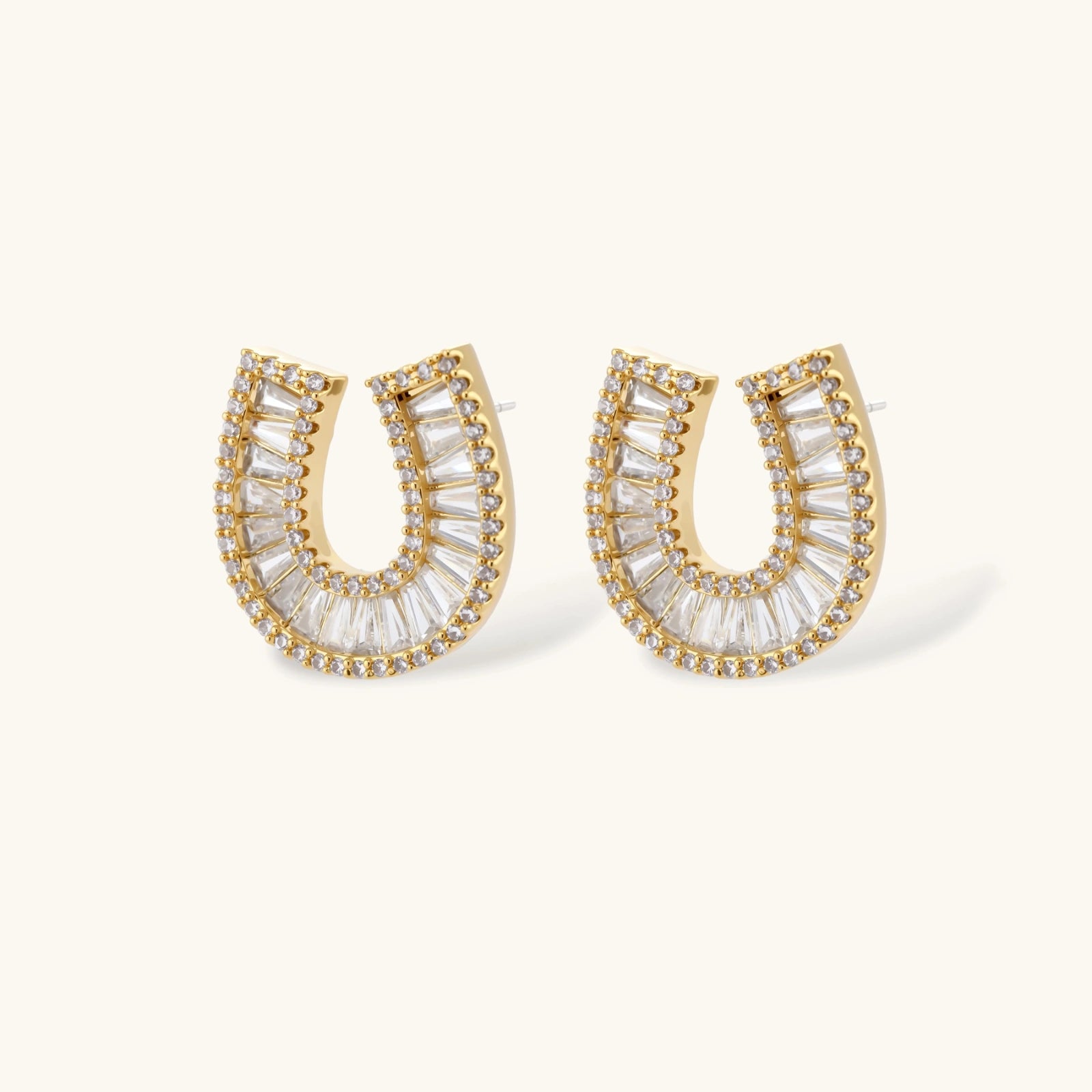 Gold-plated horseshoe necklace and earring set with baguette and round crystals arranged in geometric pattern on white background.
