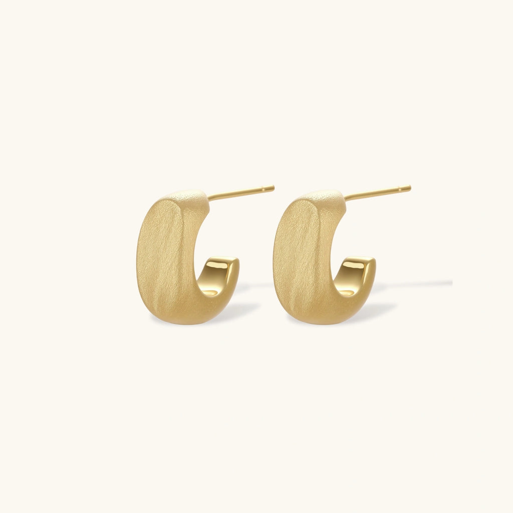 Small gold huggie earrings with matte finish, 14mm diameter, shown against cream background for everyday elegance.