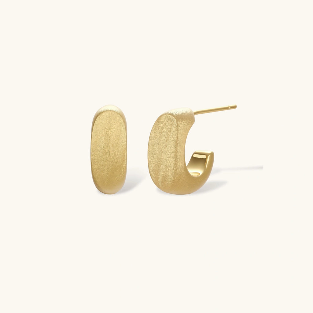 Small gold huggie earrings with matte finish, 14mm diameter, shown against cream background for everyday elegance.