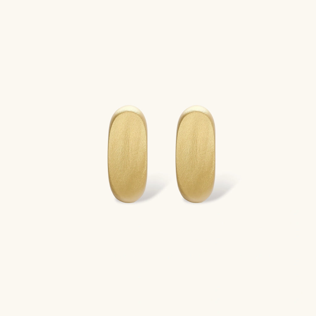Small gold huggie earrings with matte finish, 14mm diameter, shown against cream background for everyday elegance.