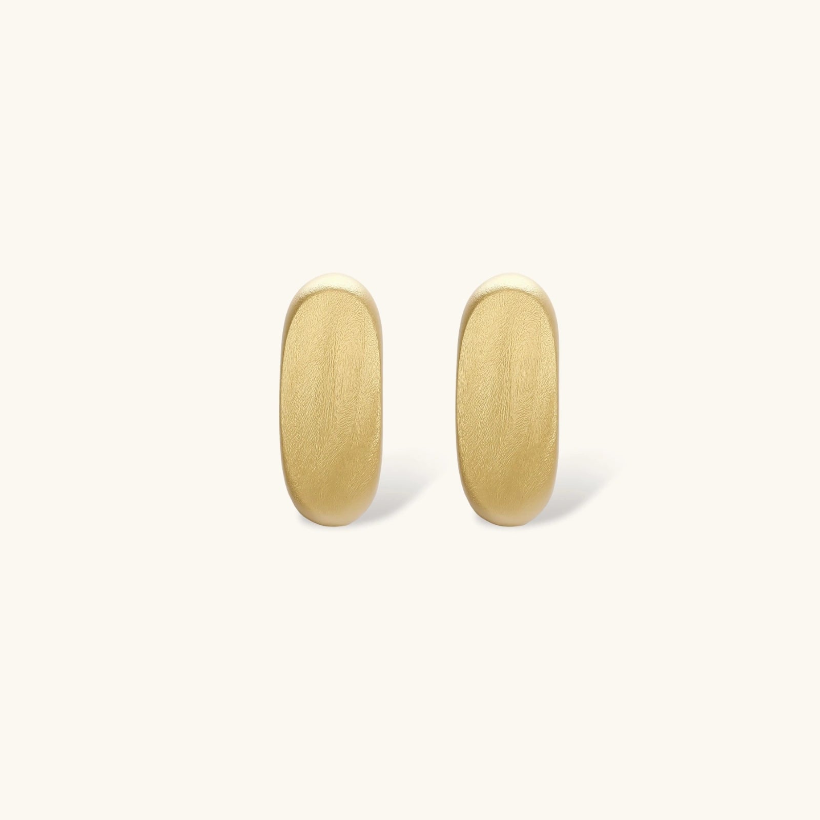 Small gold huggie earrings with matte finish, 14mm diameter, shown against cream background for everyday elegance.