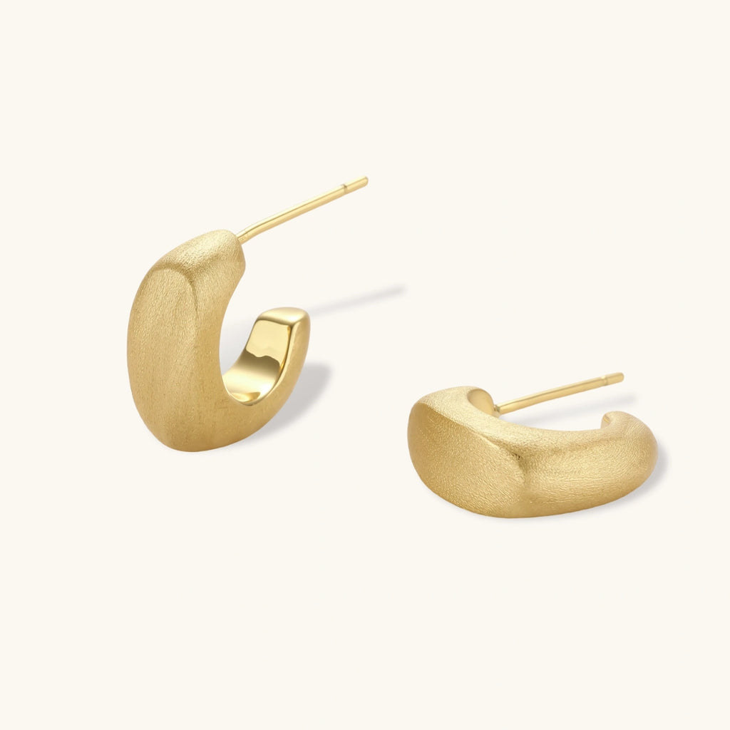 Small gold huggie earrings with matte finish, 14mm diameter, shown against cream background for everyday elegance.